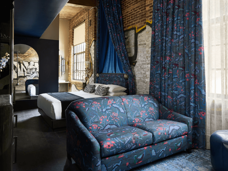 Hotel room with a king sized bed with a blue canopy, a blue couch, and a door to the bathroom Hotel room with a king sized bed with a blue canopy, a blue couch, and a door to the bathroom